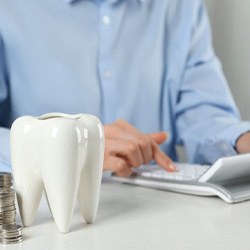 A man using a calculator near a large ceramic tooth and some silver coins