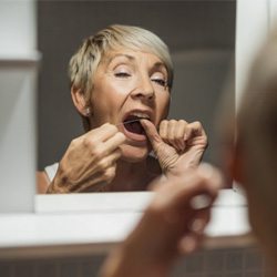 a woman flossing her dental implants to maintain them