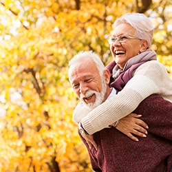 Man giving woman a piggy back ride in front of an autumn tree