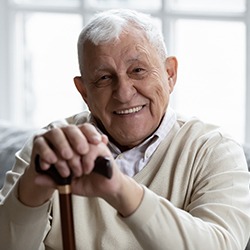 Man sitting on gray couch smiling and holding walking cane