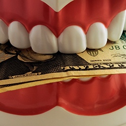 A closeup of dentures biting down on dollar bills
