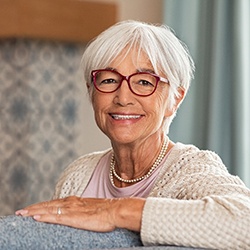 Senior woman with glasses sitting on couch and smiling