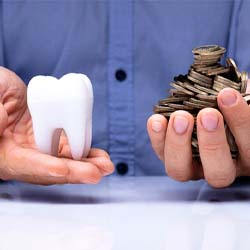 Man holding model tooth and coins in his hands