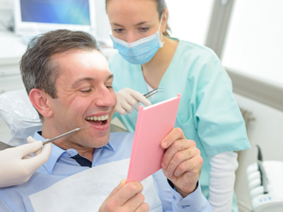 Dentist looking over man’s shoulder as he admires results in mirror