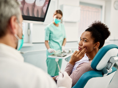 Woman in dental chair pressing two fingers to her jaw in pain