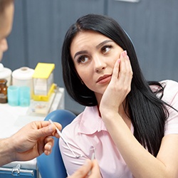 Woman in dental chair holding cheek