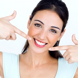 young woman pointing to her smile after getting teeth whitening in Lisle