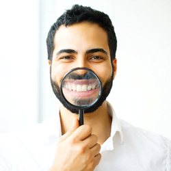 man in white dress shirt holding magnifying glass to his smile 