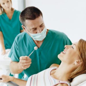 Woman Lying in a Dentist Chair With Male Dentist Sitting By Her Wearing a Face Mask; Female Dentist in the Background