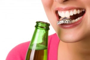 close up woman using her teeth to open a bottle