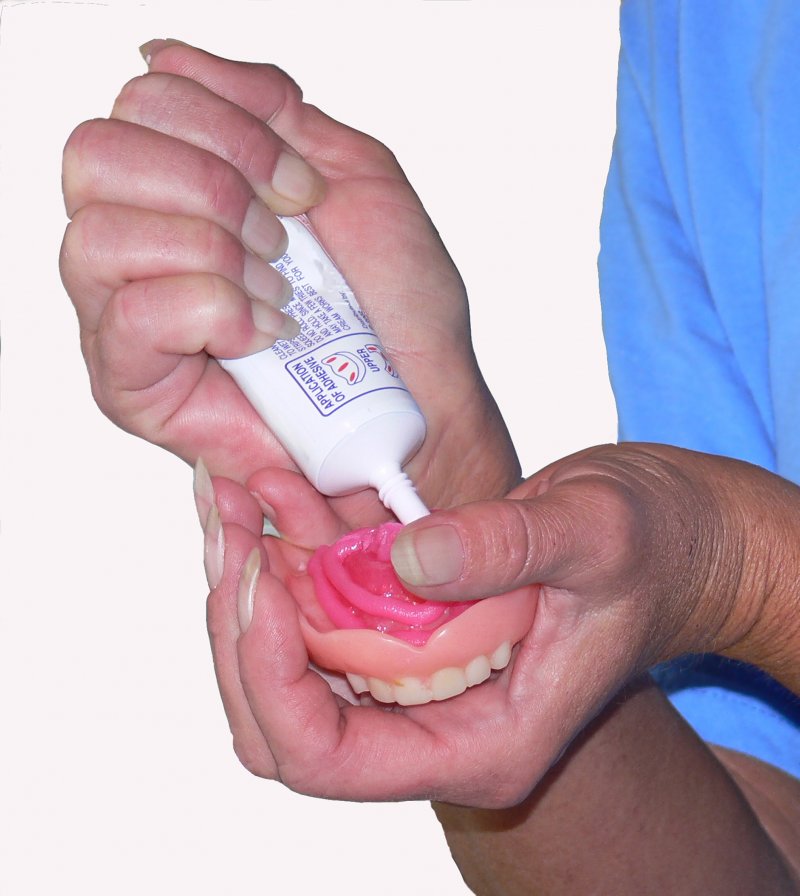 dentist putting adhesive on dentures