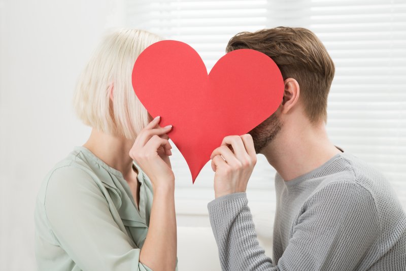 couple kissing behind paper heart