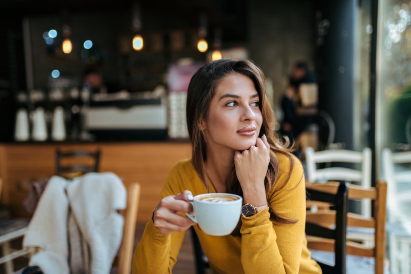 Stylish young woman drinking coffee at a cafe, looking away.