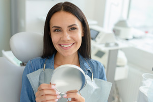 Woman sitting in dental chair holding mirror